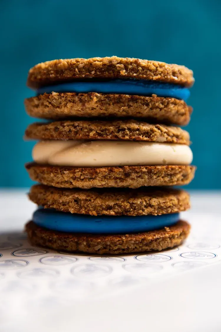 Stack of sandwich cookies with blue filling on a white surface against a teal background