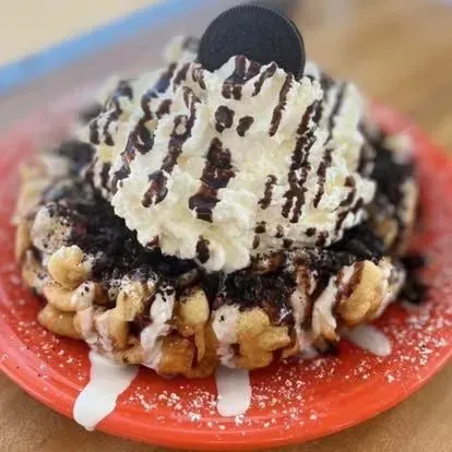 Ice cream waffle stack with whipped cream, chocolate drizzle, and an Oreo on a red plate