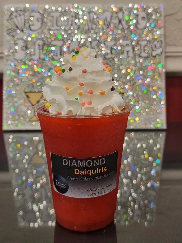 Red daiquiri drink topped with whipped cream and sprinkles in a clear cup against a sparkly silver background