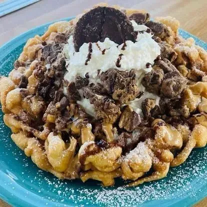 Chocolate dessert topped with whipped cream and an Oreo on a blue plate, dusted with powdered sugar