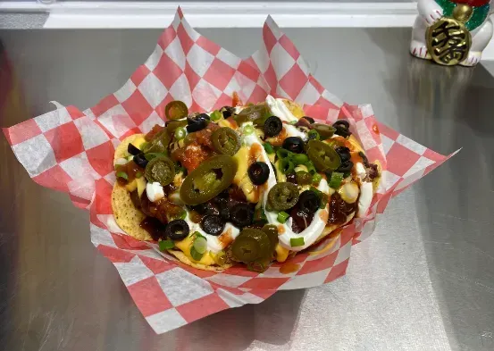 Loaded nachos topped with cheese, olives, jalapeños, and sour cream on checkered paper.