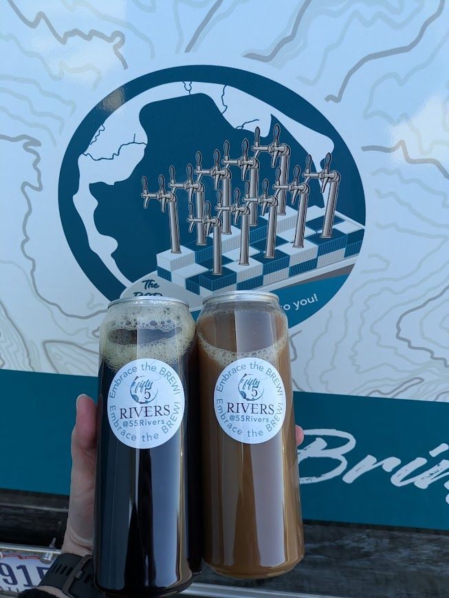 Two bottled drinks held up in front of a blue mural with industrial cranes and a map-like design