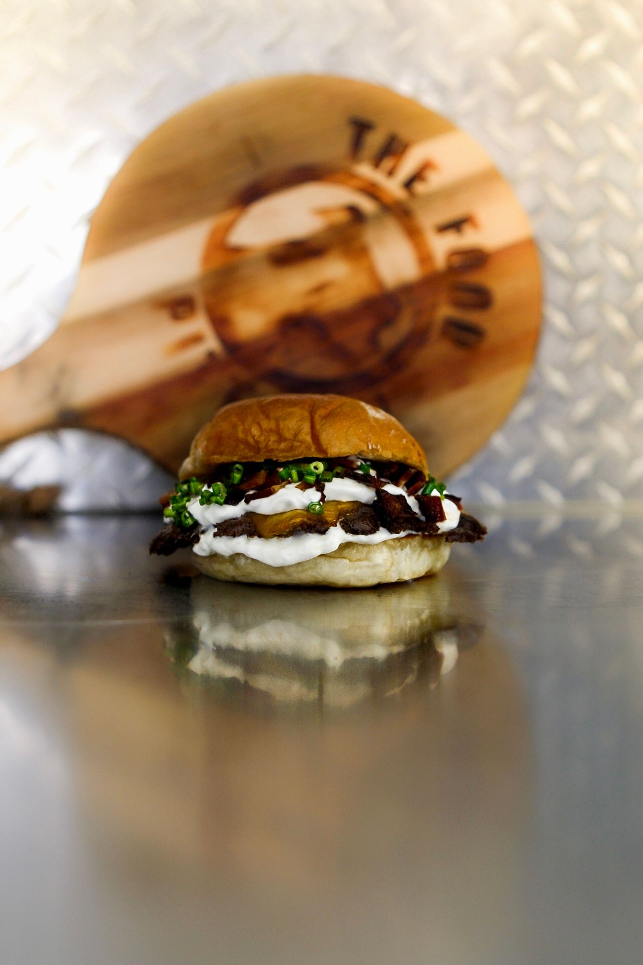 Mini burger on a reflective metal counter with a blurred circular logo in the background