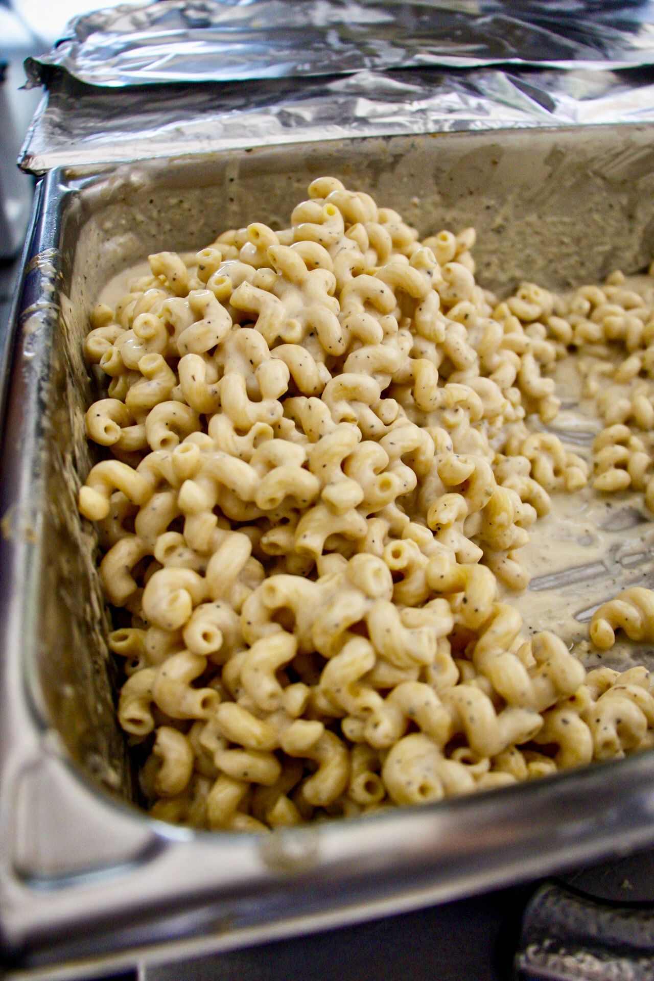 Tray of elbow macaroni pasta in a foil pan, topped with creamy sauce or cheese.