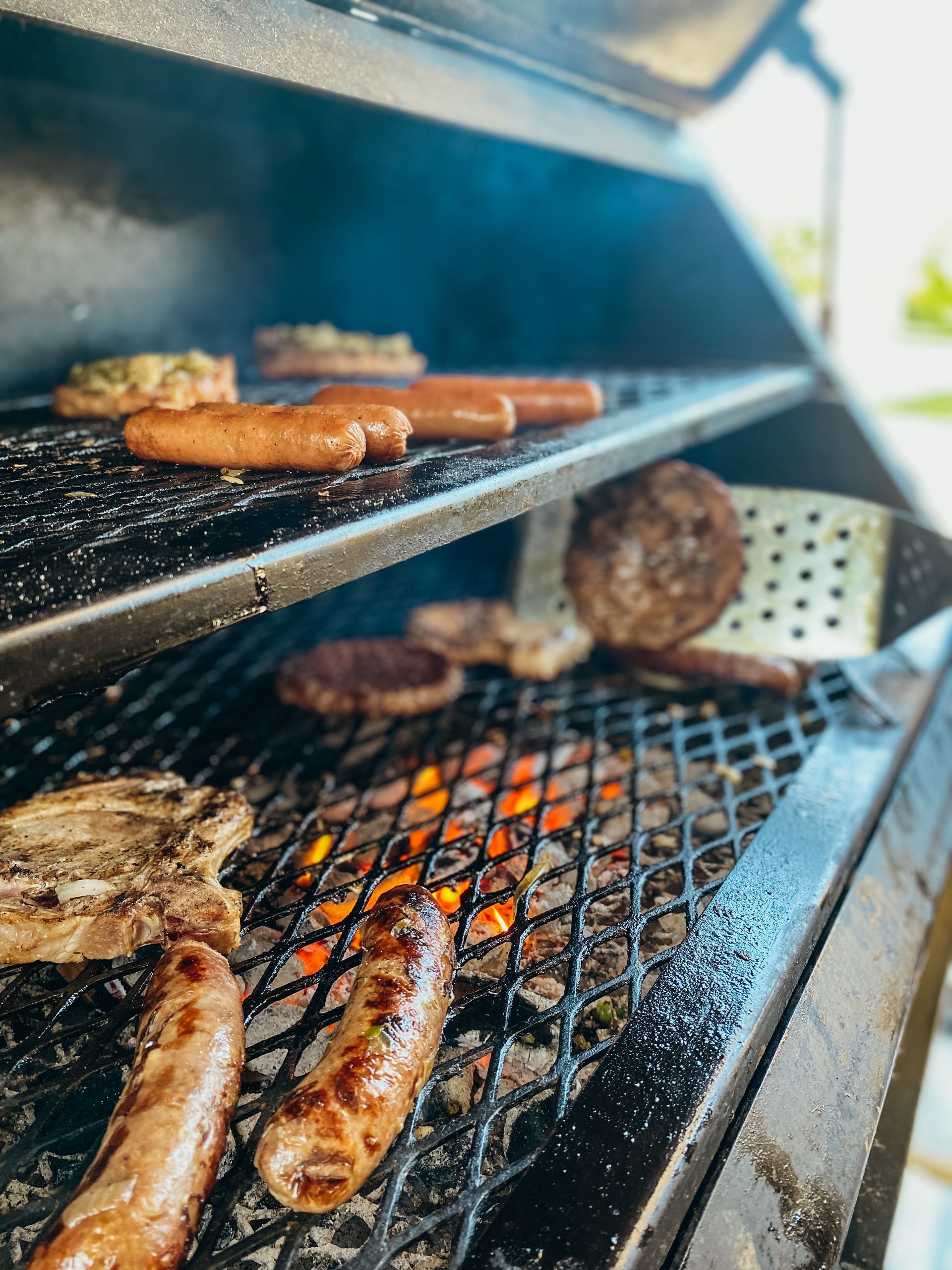 Assorted sausages and burger patties grilling over open flames on a barbecue