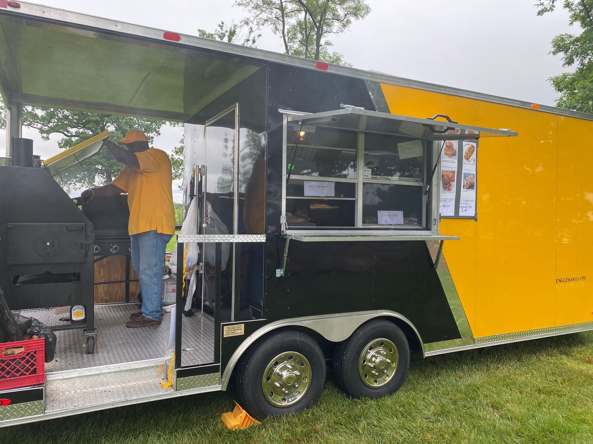 Food truck with open serving window, yellow and black exterior, parked on grass with a person inside