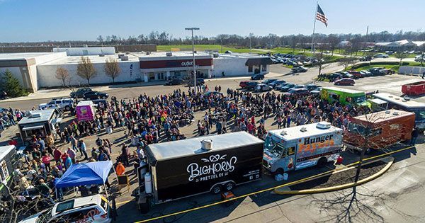 Crowd gathered outside a store at a food truck event with several trucks and tents on a sunny day