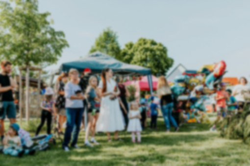 People gathered outdoors at a colorful community festival with tents, tables, and bicycles on a grassy field.
