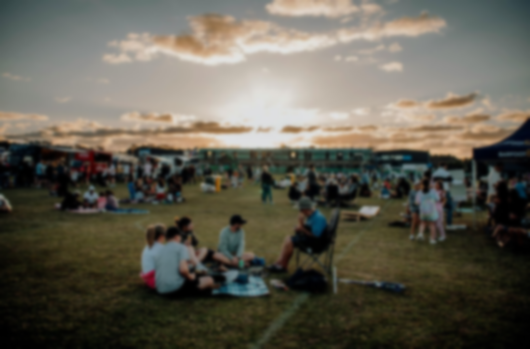 People sitting on blankets at an outdoor sunset gathering in a grassy field.