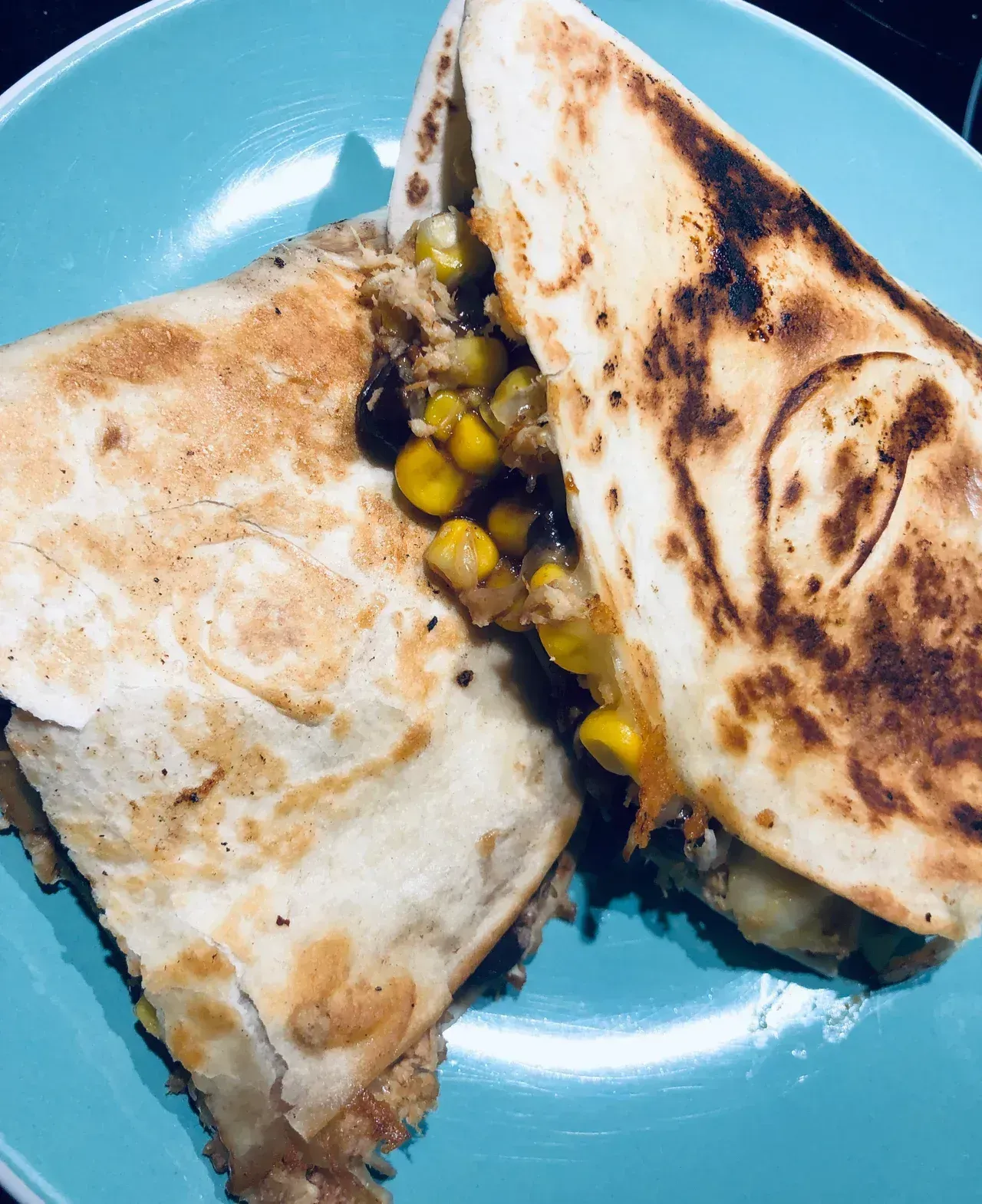 Two toasted quesadillas on a blue plate with corn filling visible between them