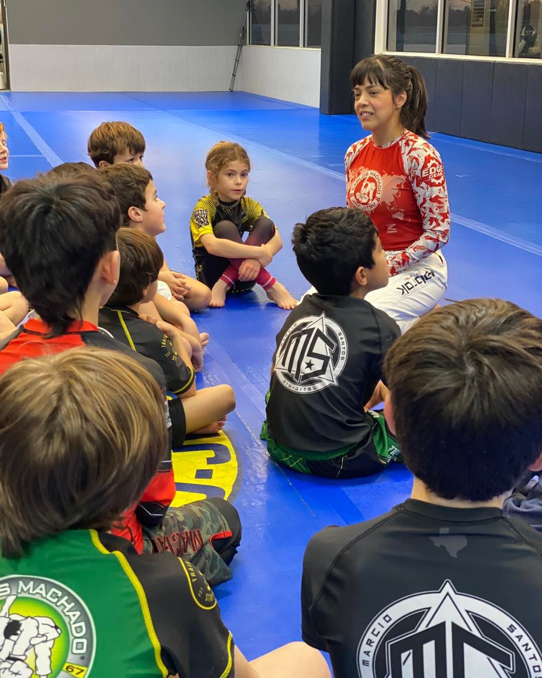 a woman is talking to a group of children who are sitting on the floor .