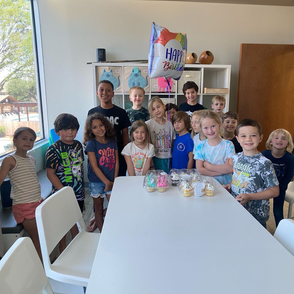 a little girl wearing a party hat is opening a gift box at a birthday party .