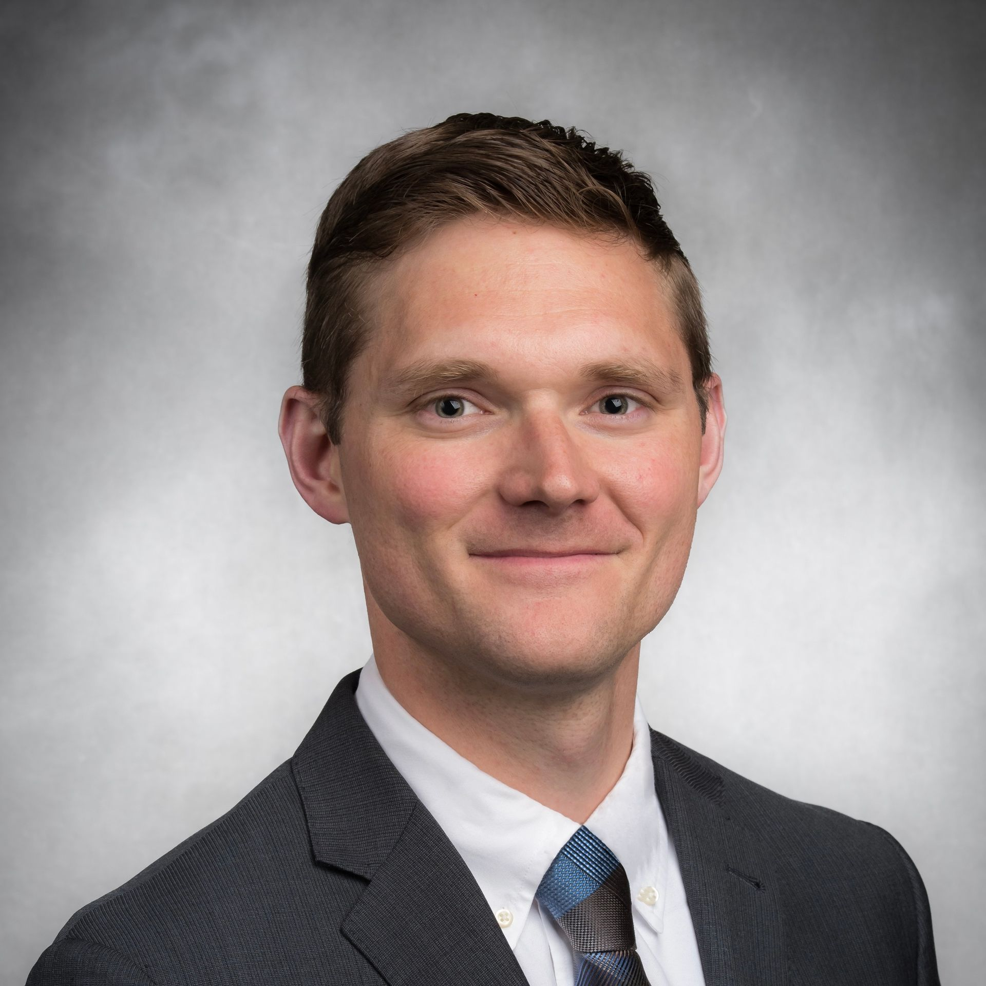 Man in suit smiles, facing forward; neutral background.