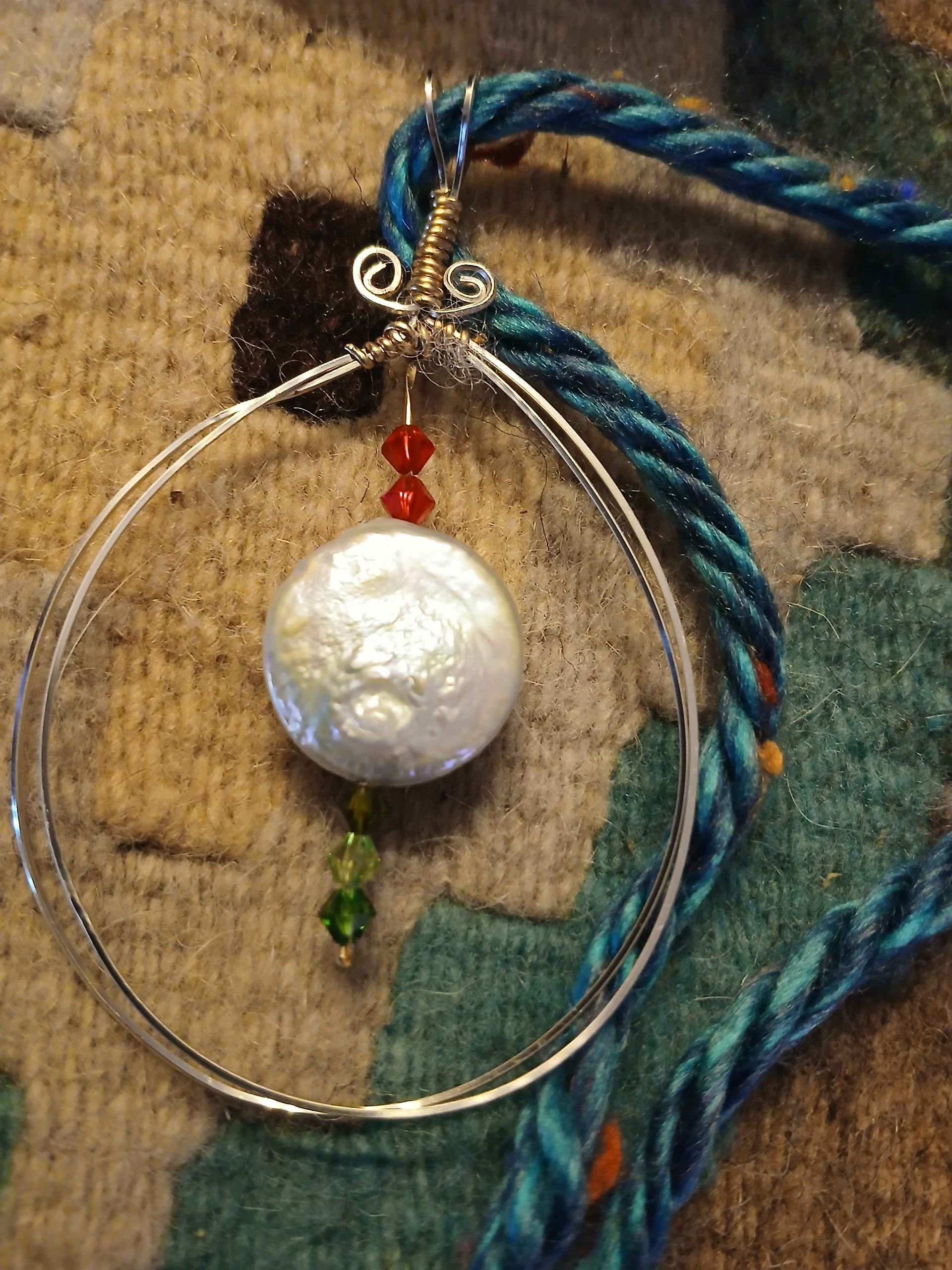 A necklace with a pearl and beads is sitting on a rug.