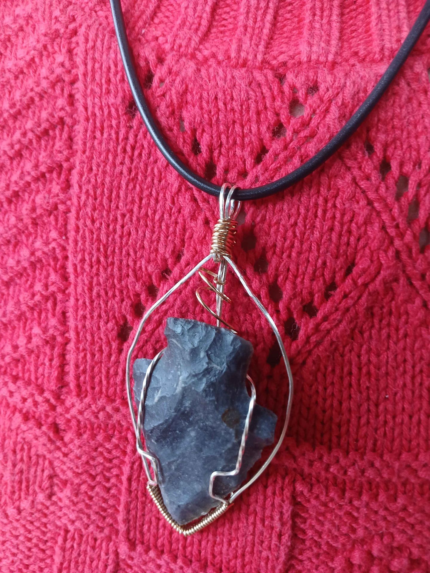 A close up of a necklace with a black stone pendant on a red sweater.