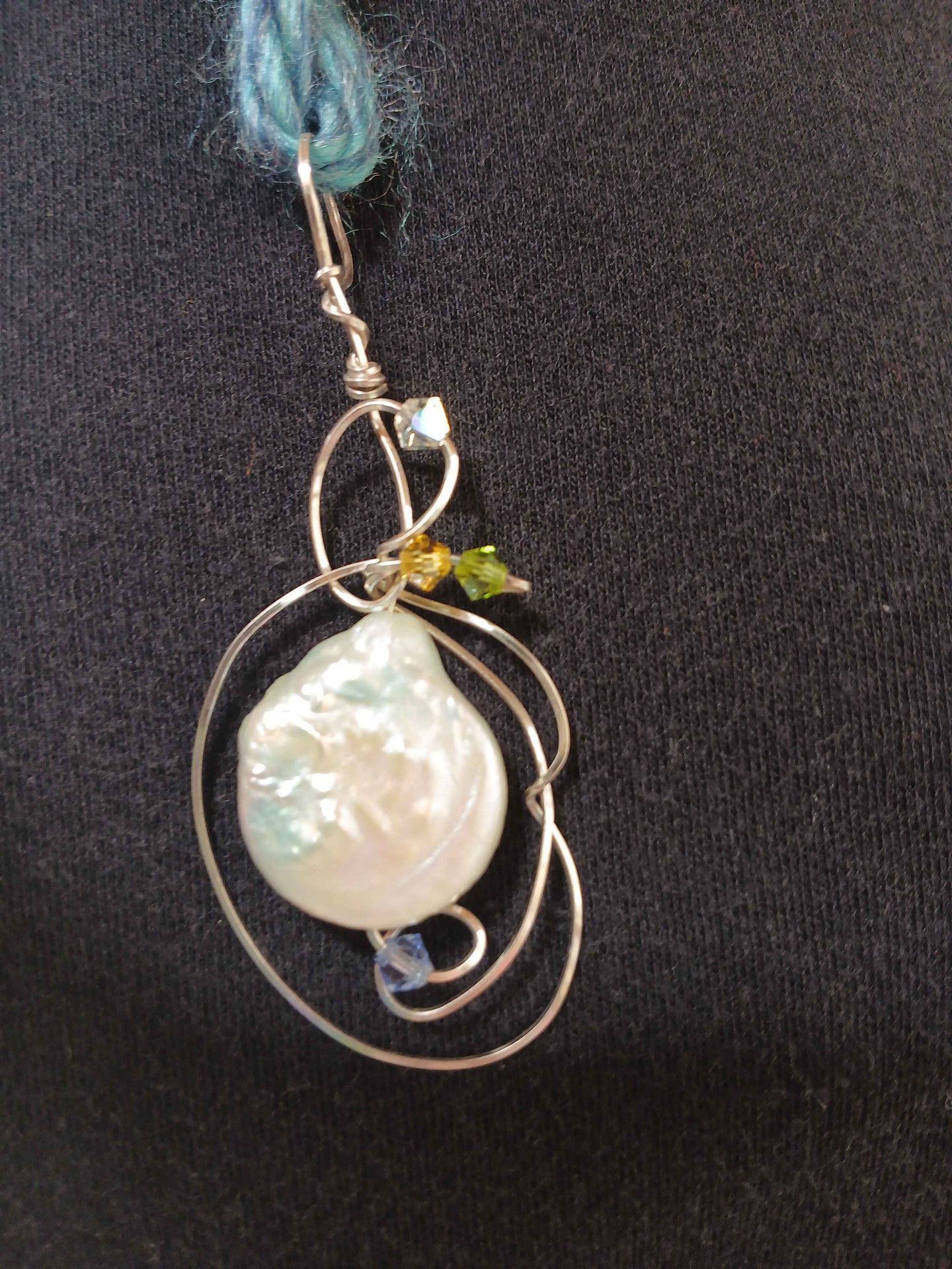 A close up of a necklace with a pearl and beads on a black background.