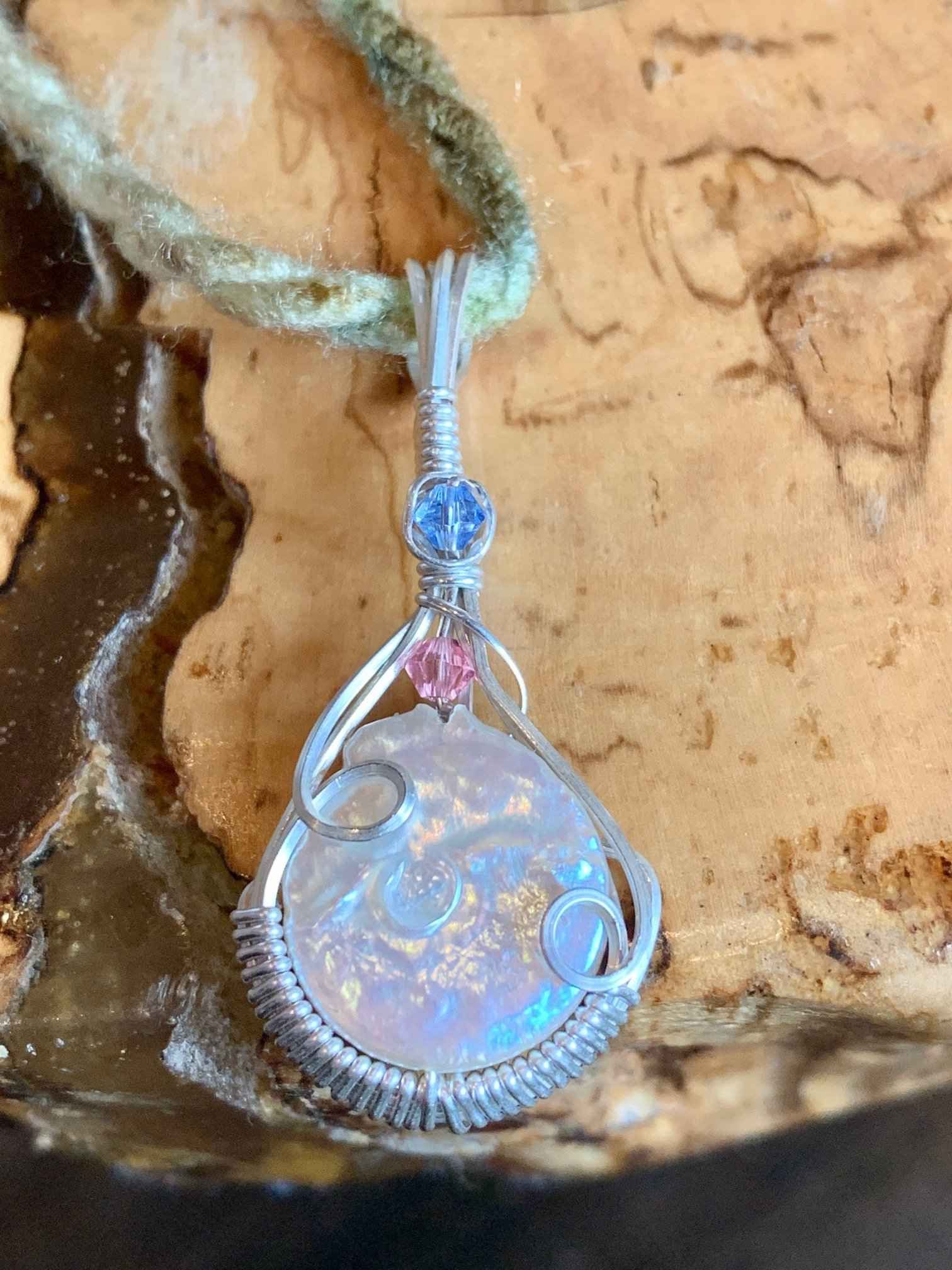 A wire wrapped pendant is sitting on top of a piece of wood.