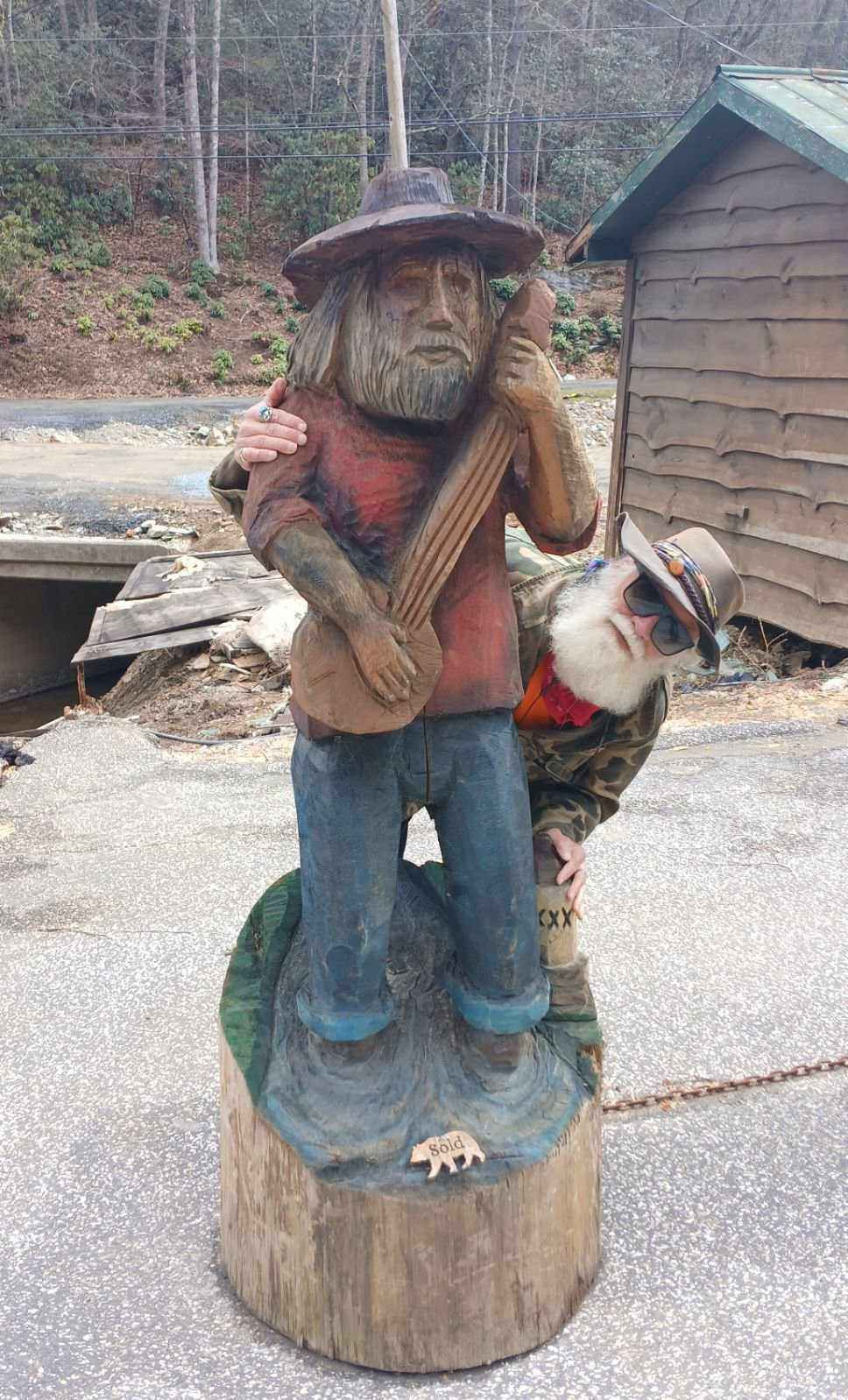 A wood carving of a man playing a guitar on a tree stump.