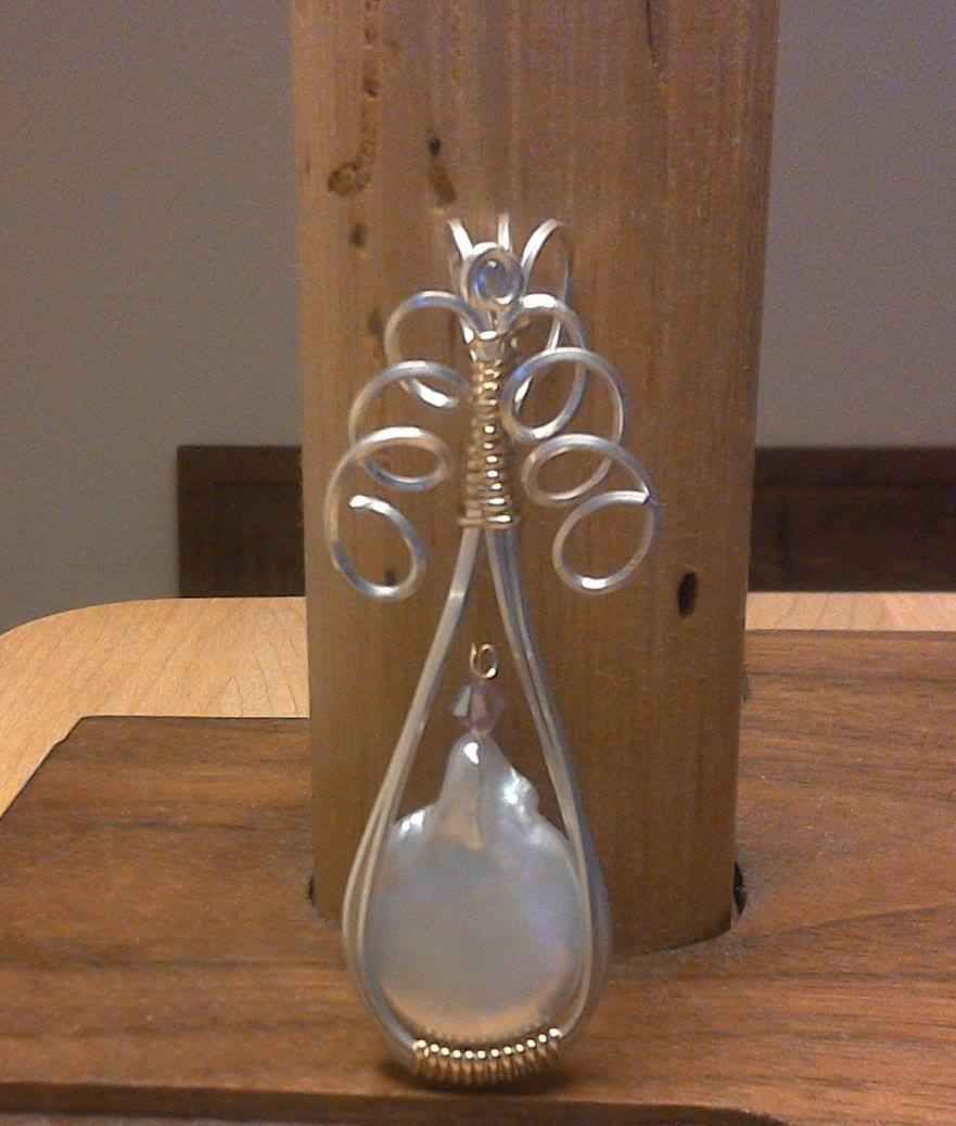 A wire wrapped pendant with a pearl in it is sitting on a wooden table