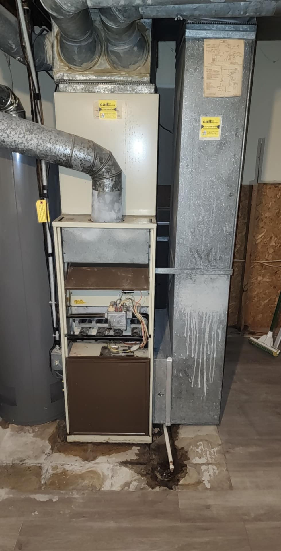A dirty air conditioner is sitting in a basement next to a water heater.