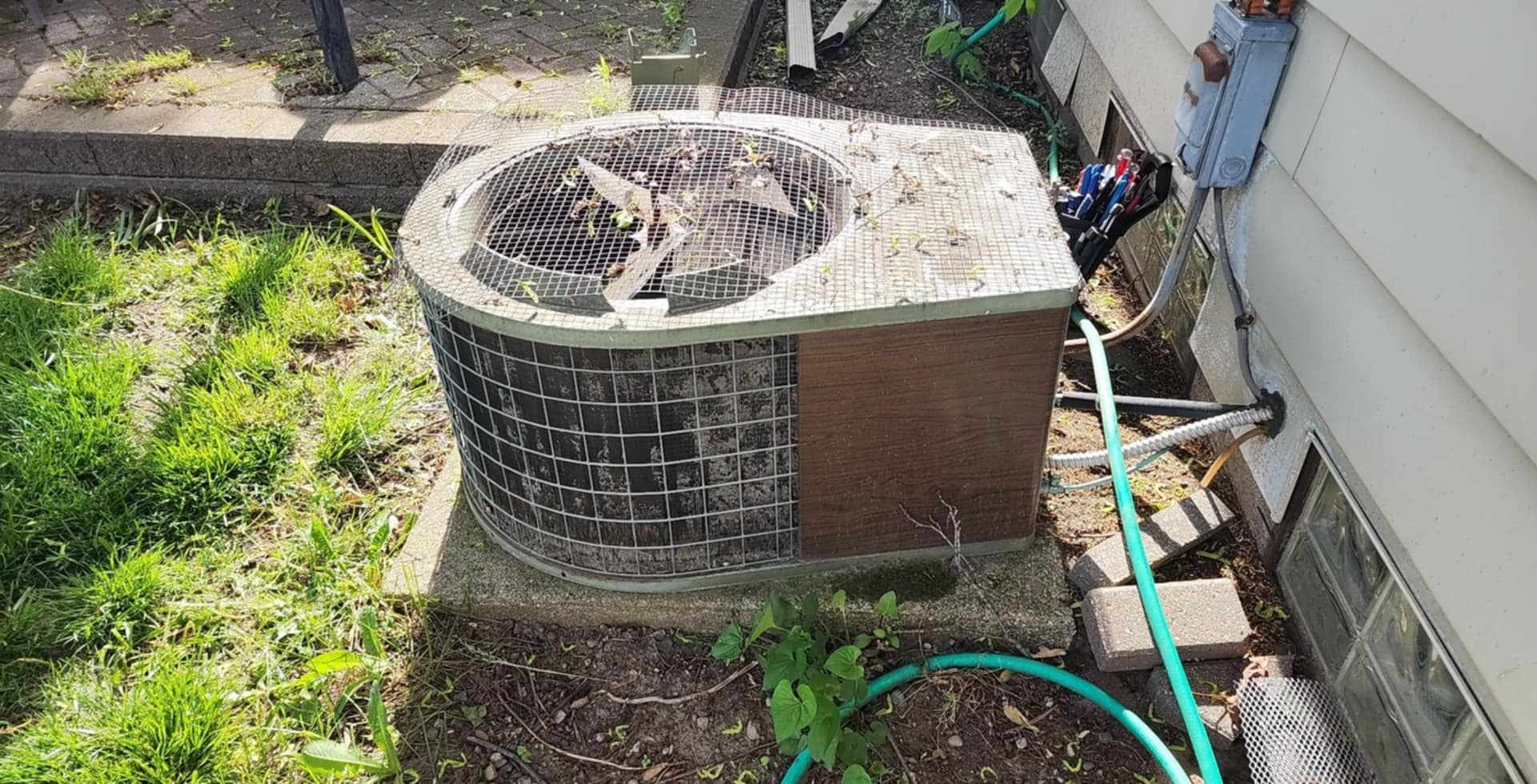 An air conditioner is sitting on the side of a house next to a hose.