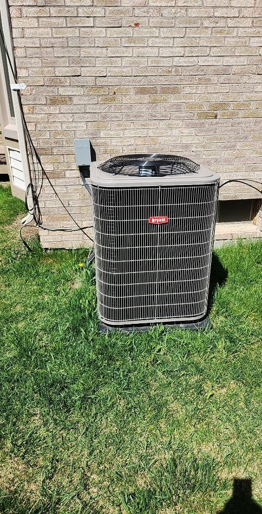 An air conditioner is sitting in the grass in front of a brick building.
