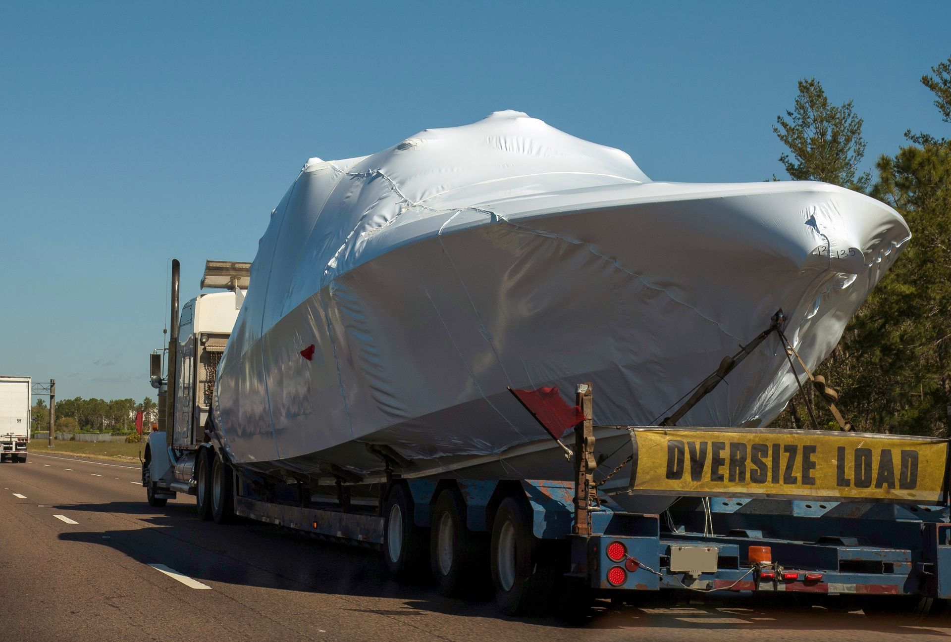 A large white boat wrapped in plastic is transported on a truck with an
