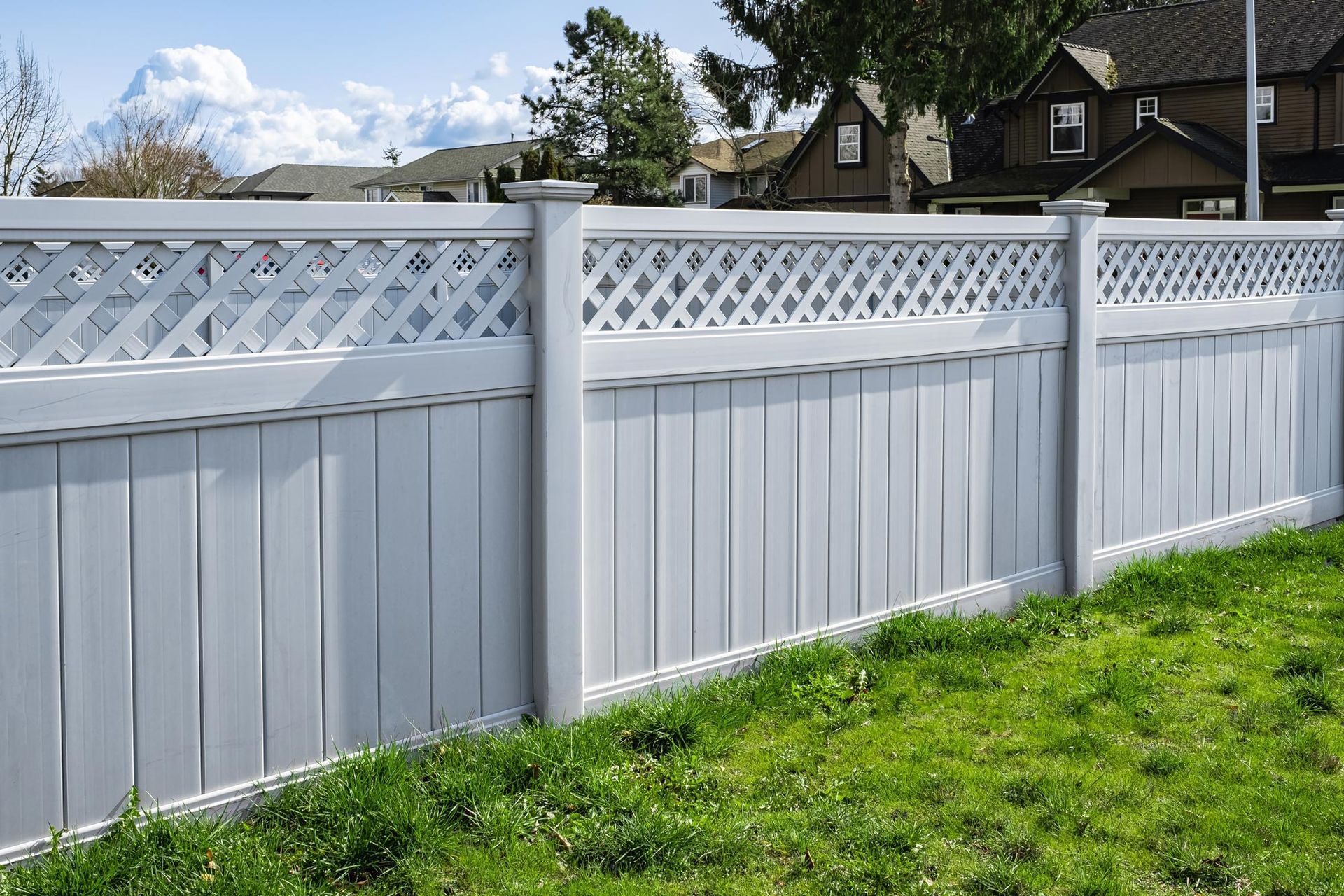 A white fence with a lattice design is surrounded by green grass.