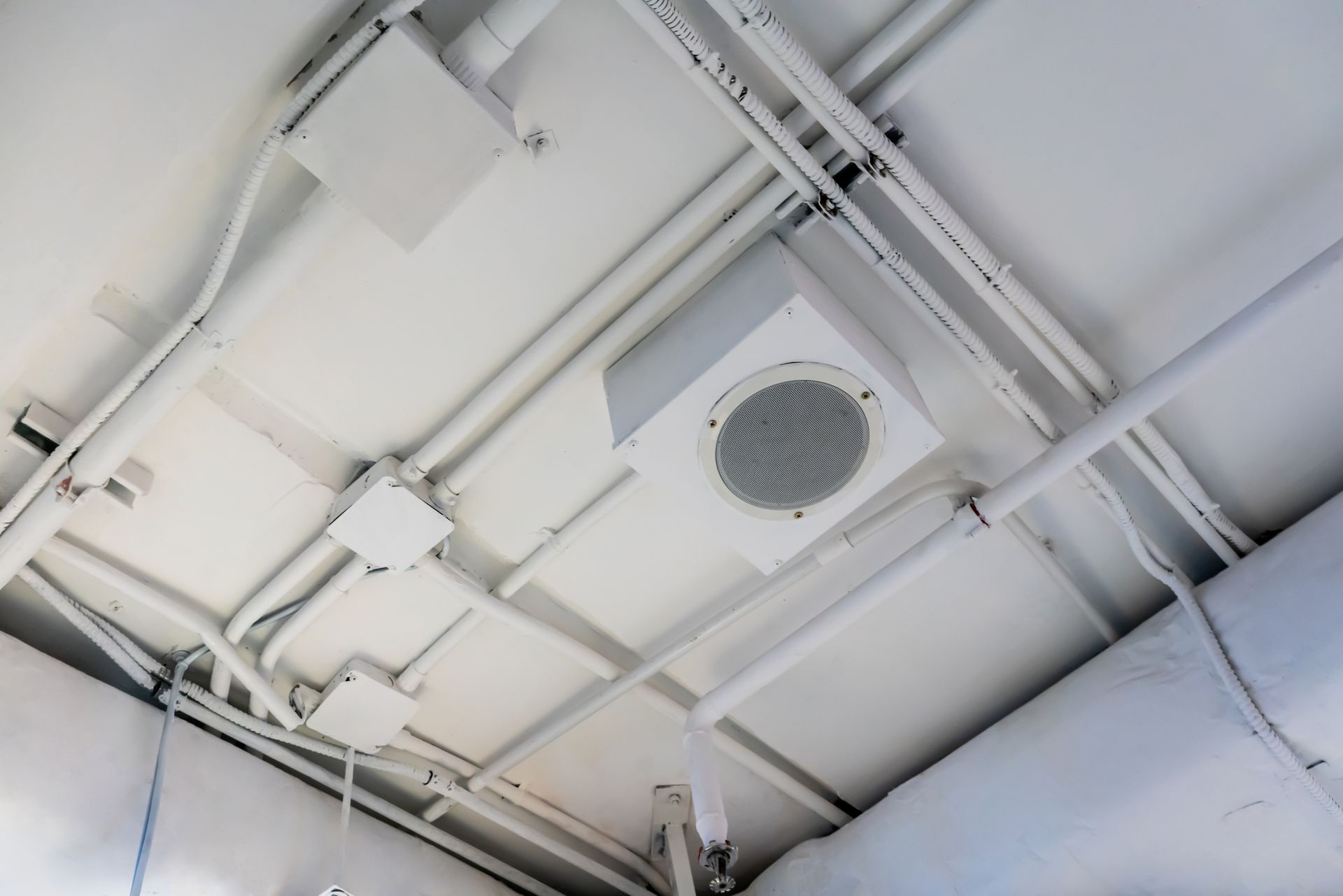 A white ceiling with pipes and a speaker on it.