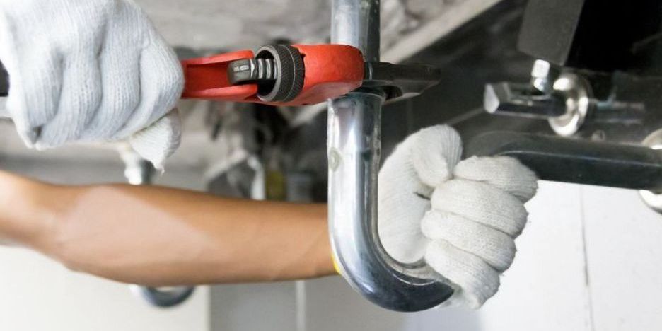 A plumber is fixing pipes with a wrench.