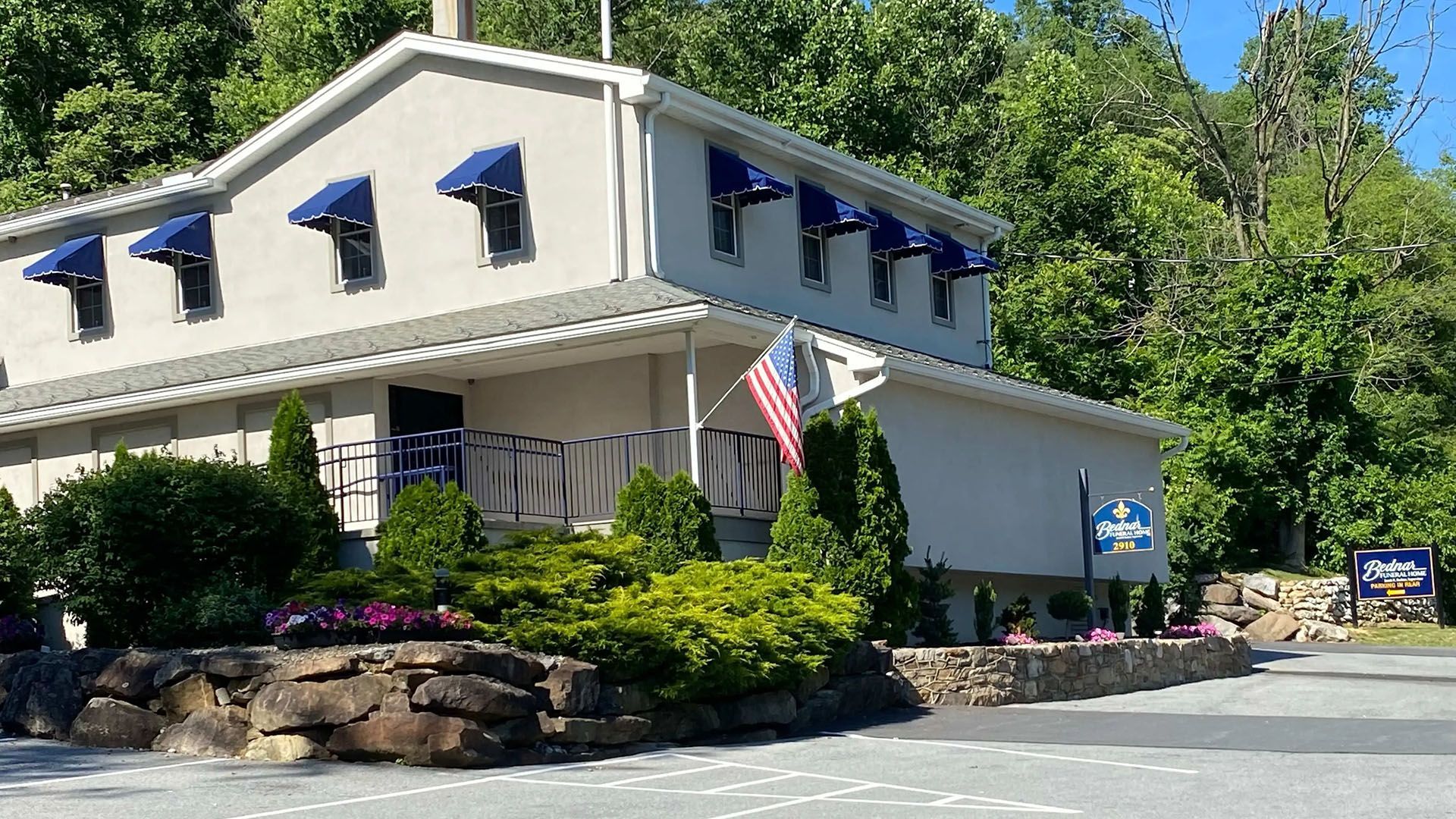Building with blue awnings, American flag, sign, surrounded by greenery.