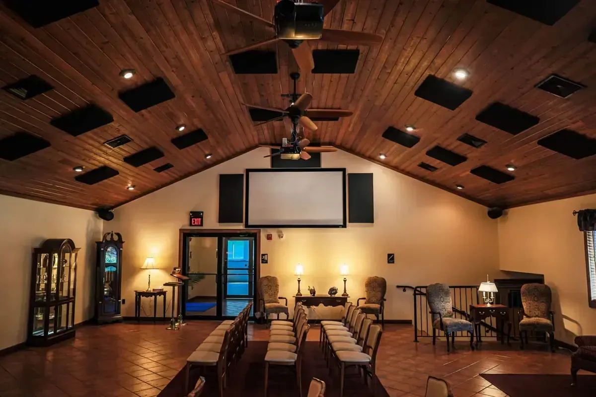 Interior view of a room with a sloped wooden ceiling, chairs in rows, and a projector screen.