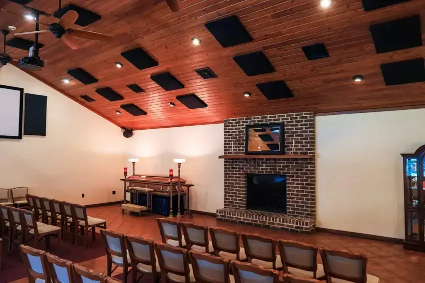A chapel interior with wooden ceiling and flooring, a brick fireplace, and seating arranged in rows.