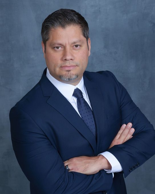 Man in a dark suit with crossed arms, looking at the camera. He has short hair and a goatee.