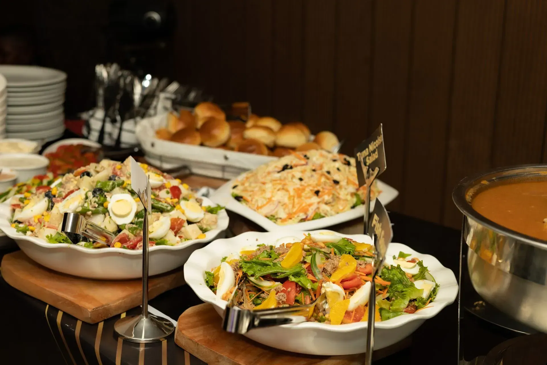 Buffet table with salads, bread rolls, and a pot of soup in a warm indoor dining setting