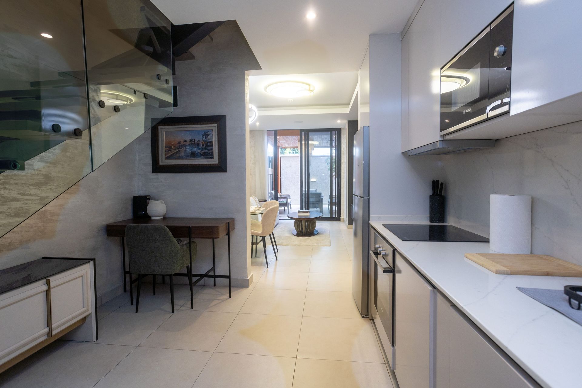 Modern hallway kitchen with glossy cabinets, tiled floor, and a small dining nook beside a staircase