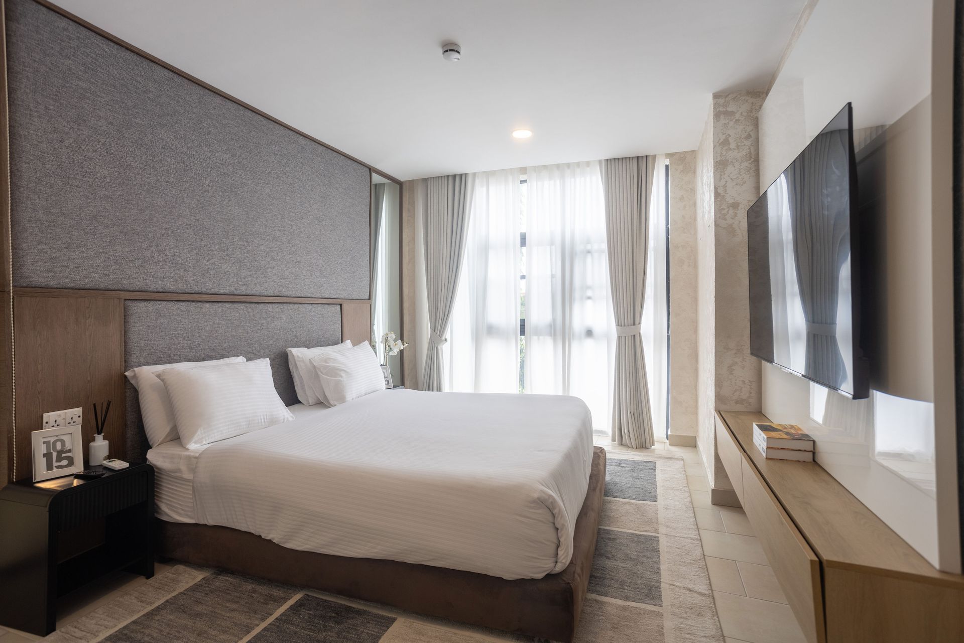 Modern hotel bedroom with a large bed, wall-mounted TV, and bright window drapes
