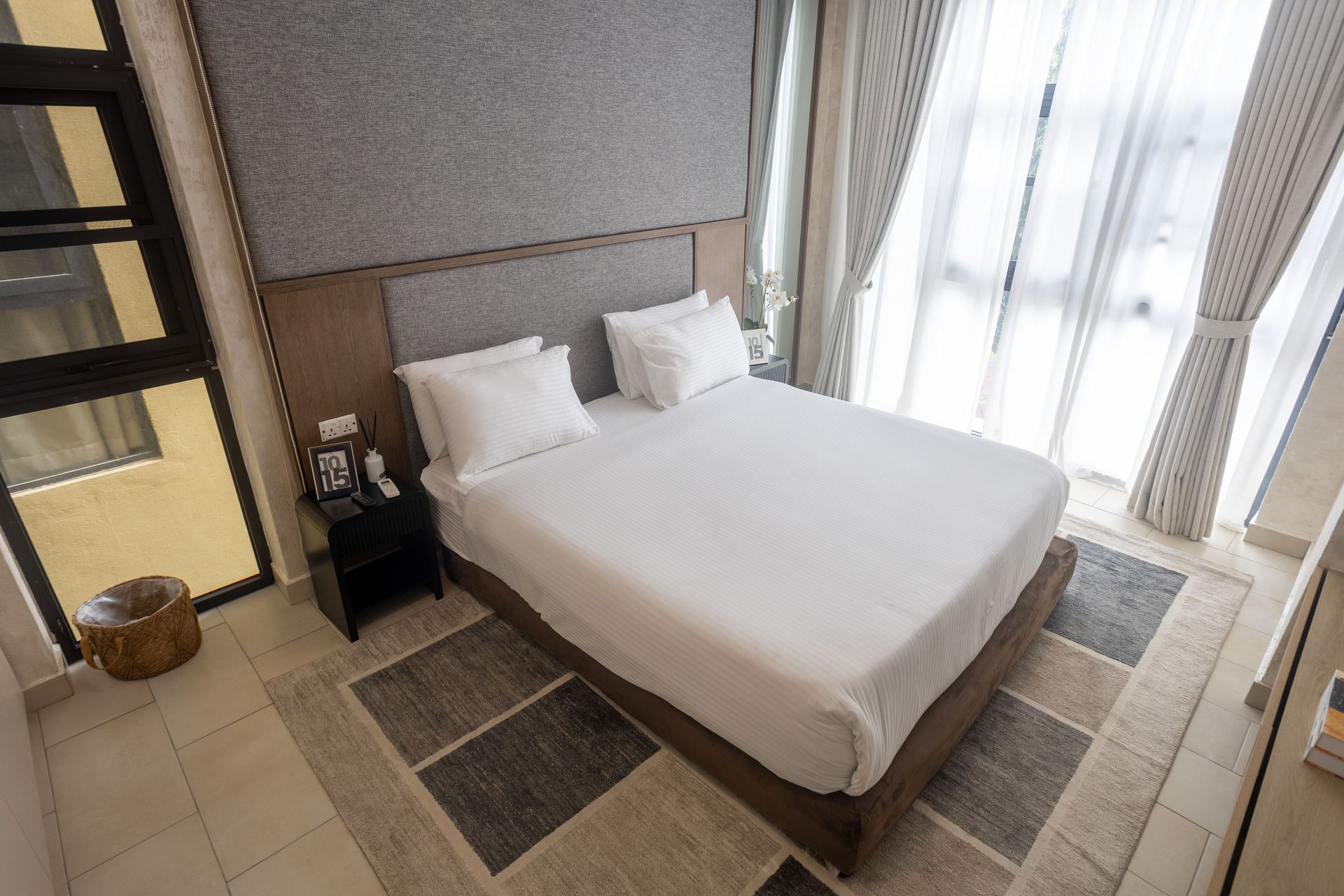 Modern hotel room with a neatly made bed, bedside table, and bright floor-to-ceiling windows