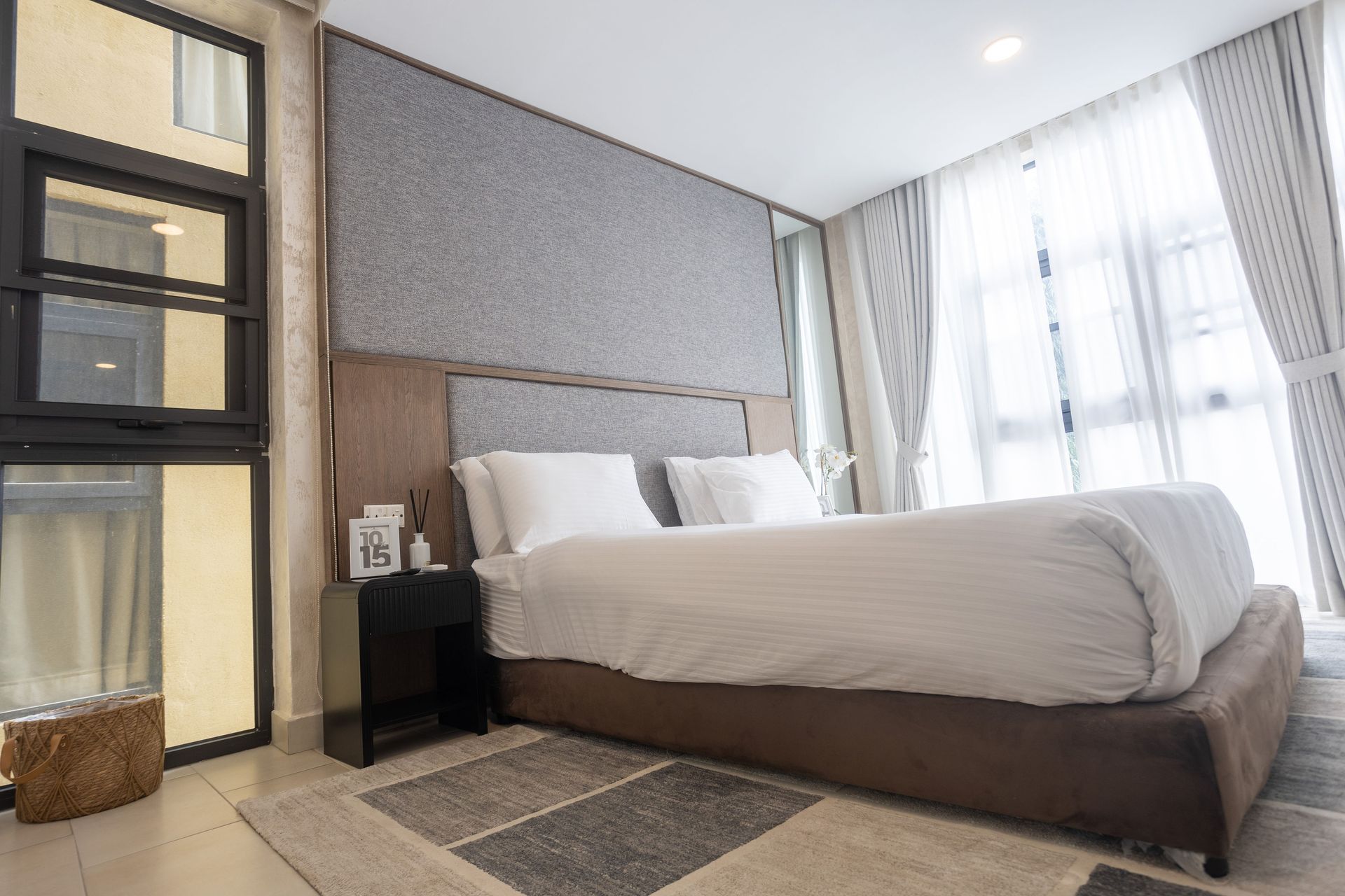 Modern bedroom with a neatly made bed, neutral decor, and large window with sheer curtains