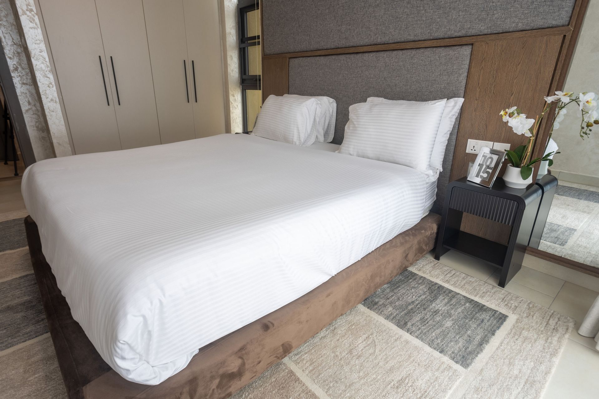 Modern bedroom with a large white bed, beige headboard, and bedside table with flowers and decor