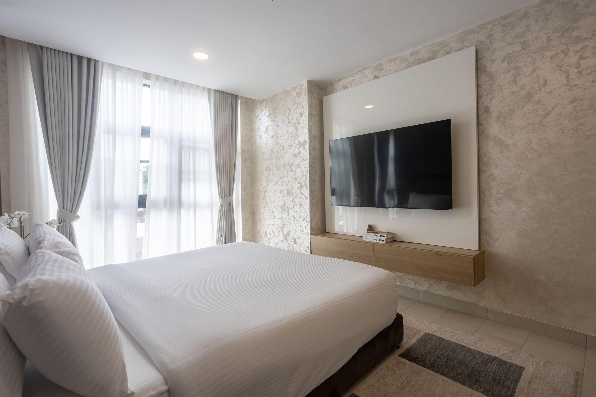 Modern bedroom with a bed, wall-mounted TV, and bright window with curtains