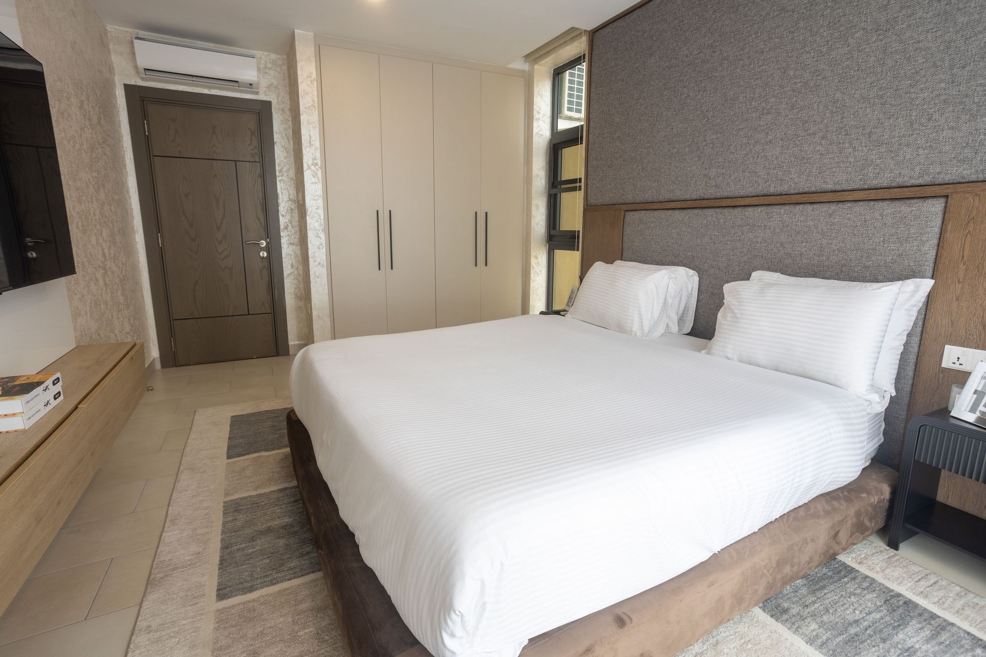 Modern hotel bedroom with a neatly made white bed, wardrobe, and window.