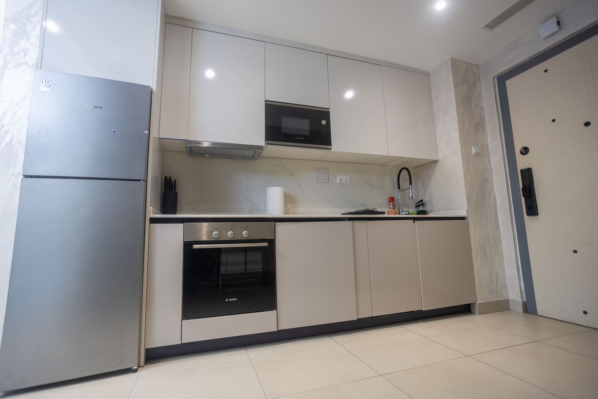 Modern kitchen with white cabinets, stainless fridge, built-in oven, and microwave in a bright tiled room