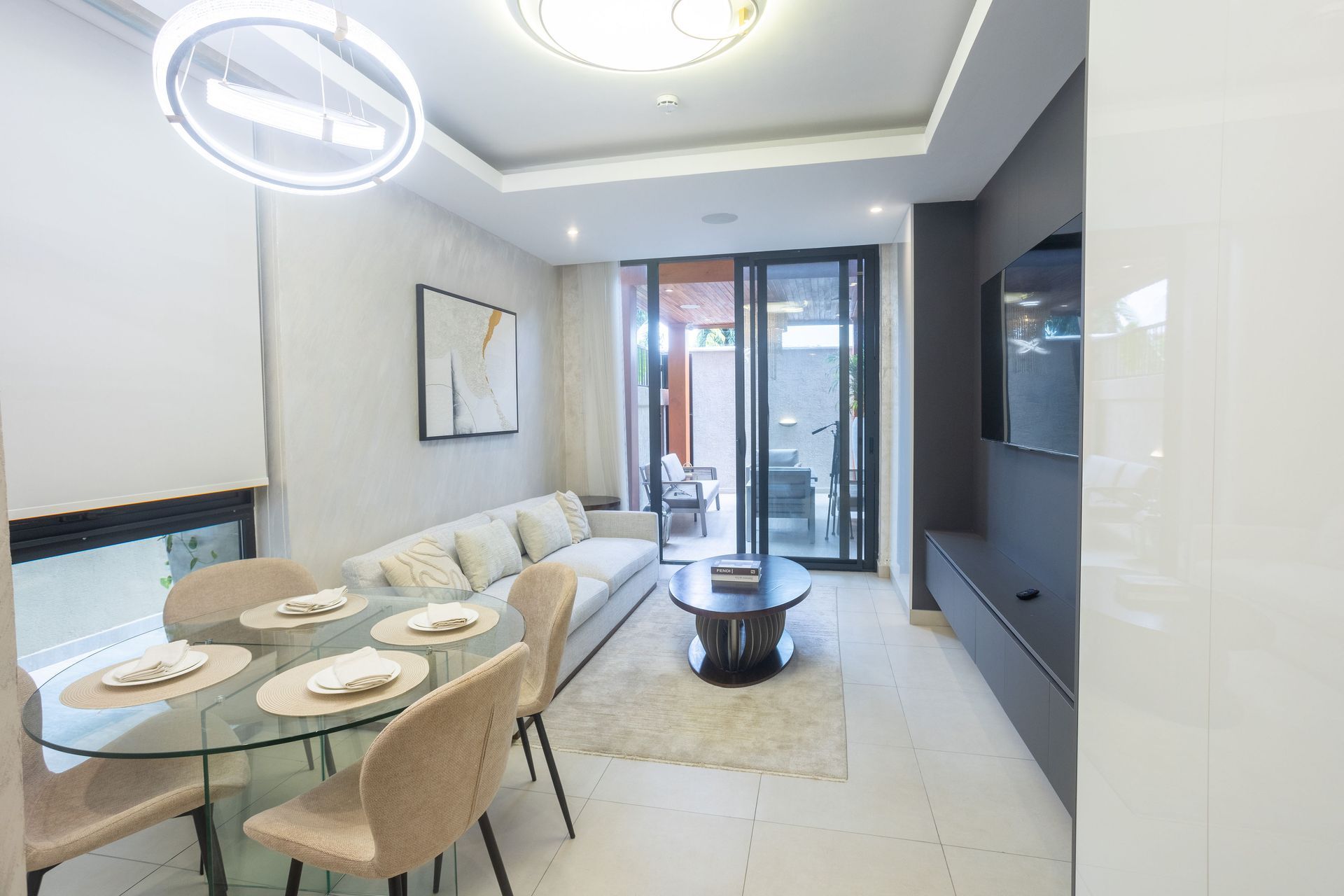 Modern dining area with a glass table, beige chairs, sofa, and sliding doors to a balcony.