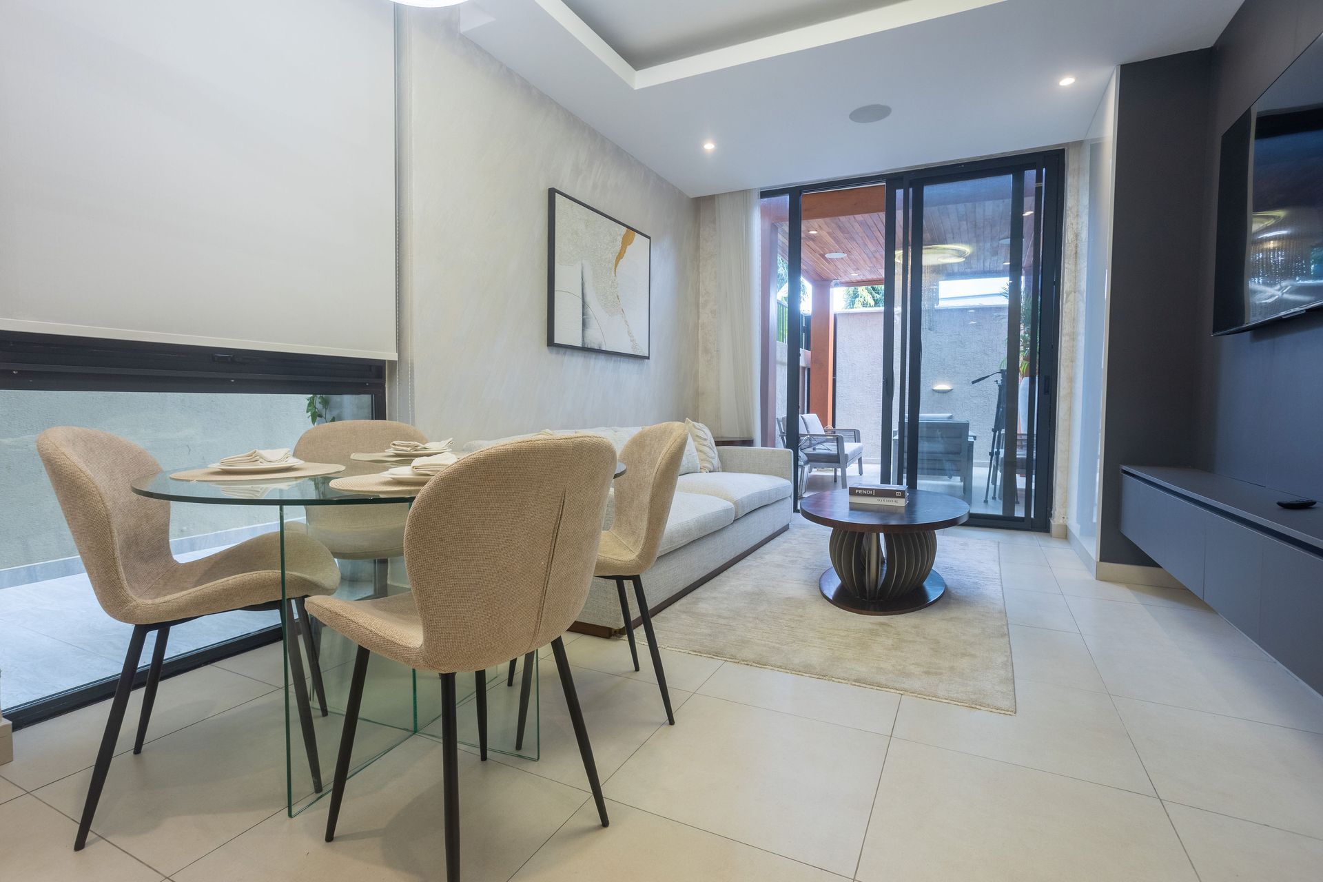 Modern dining and living room with beige chairs, glass table, gray sofa, and sliding doors to a balcony