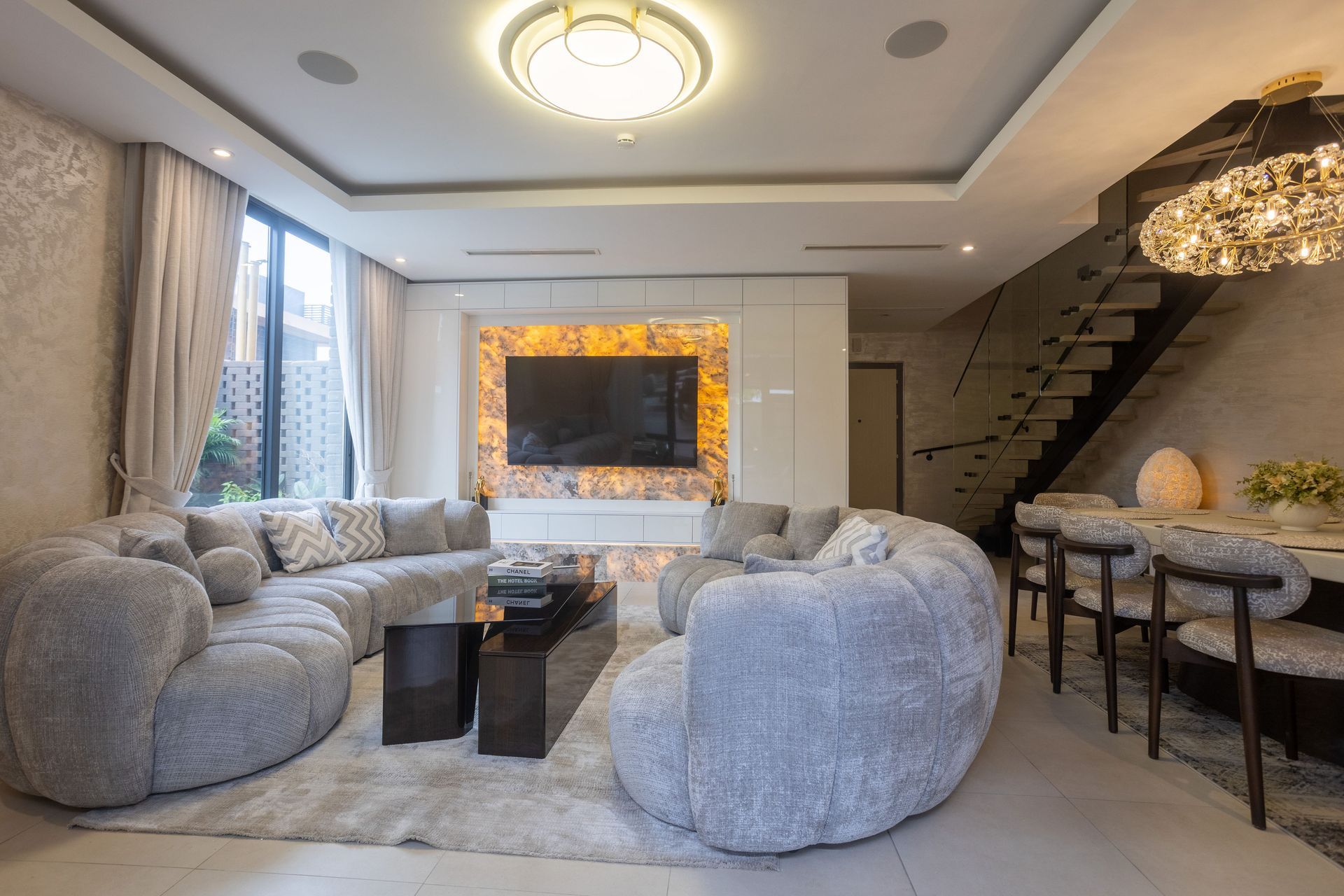 Modern living room with gray sofas, black coffee tables, warm lighting, and a staircase on the right