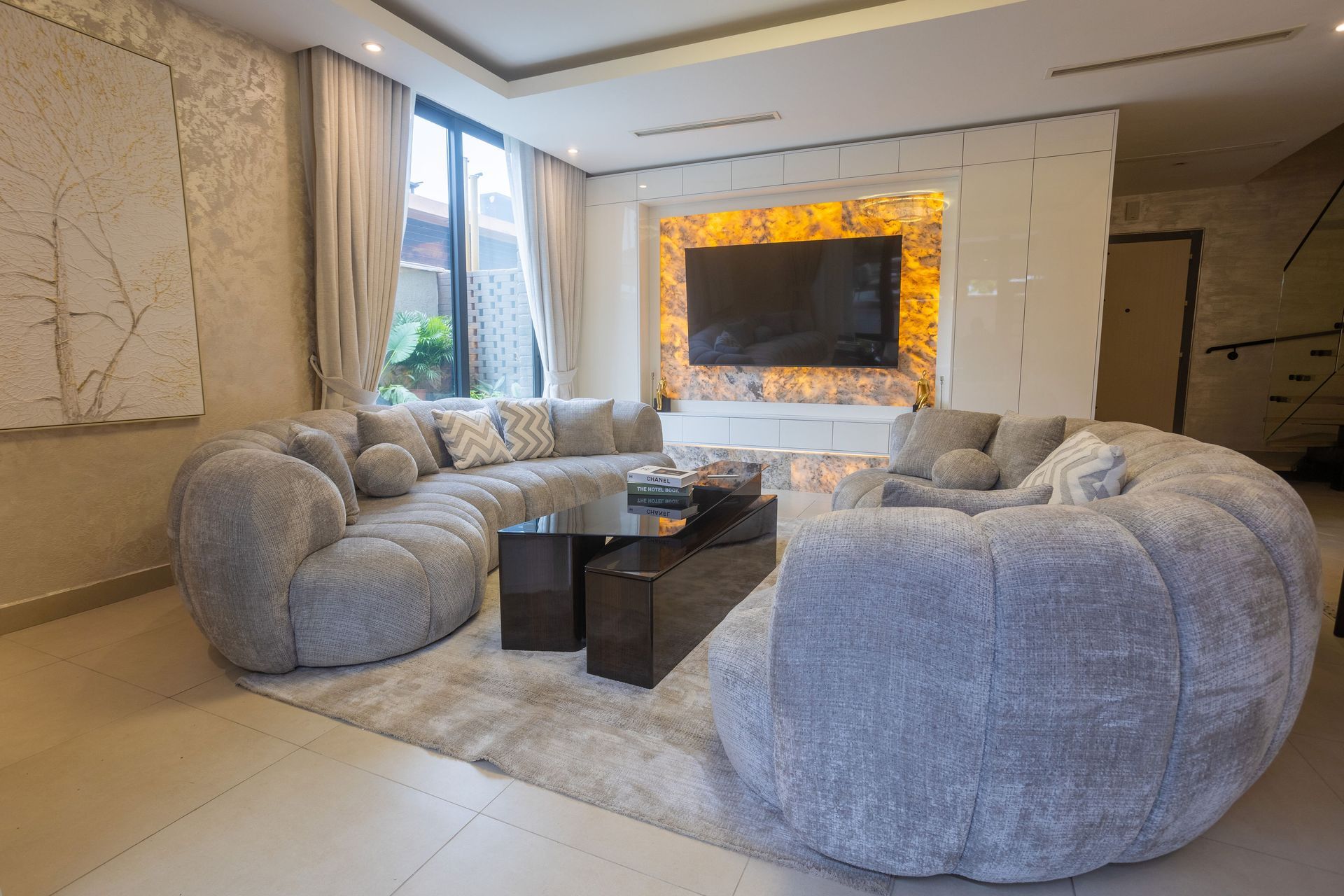 Modern living room with gray circular sofas, dark coffee tables, and a lit fireplace by a window