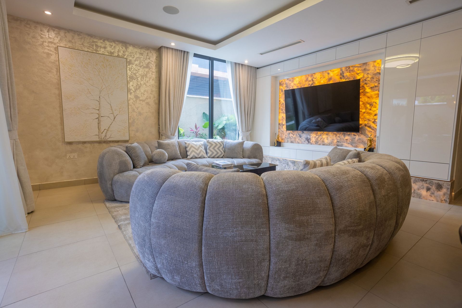 Modern living room with round gray sofas, marble floor, and a wall-mounted TV with warm backlighting