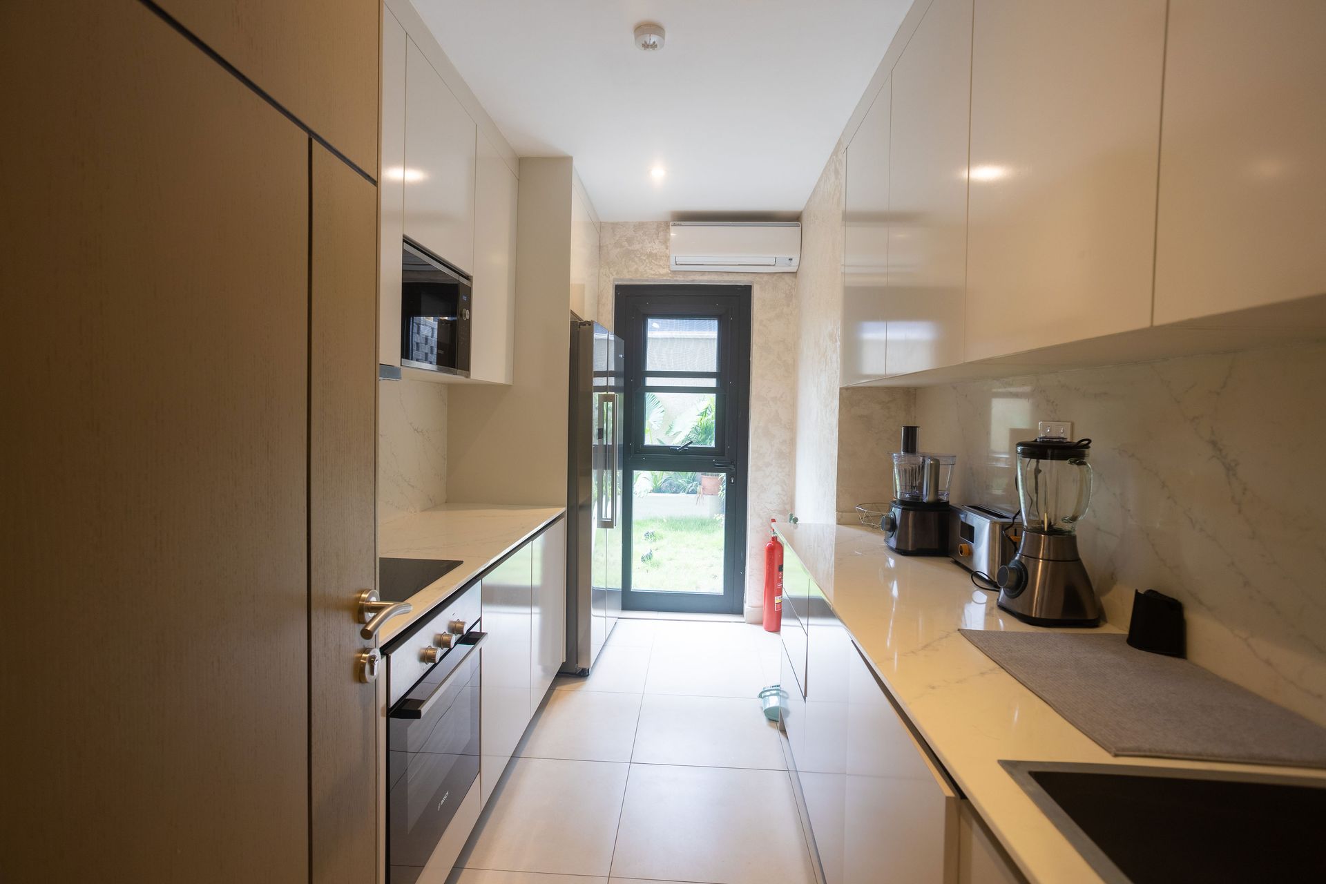 Narrow modern galley kitchen with light cabinets, white countertops, and a glass door at the end.