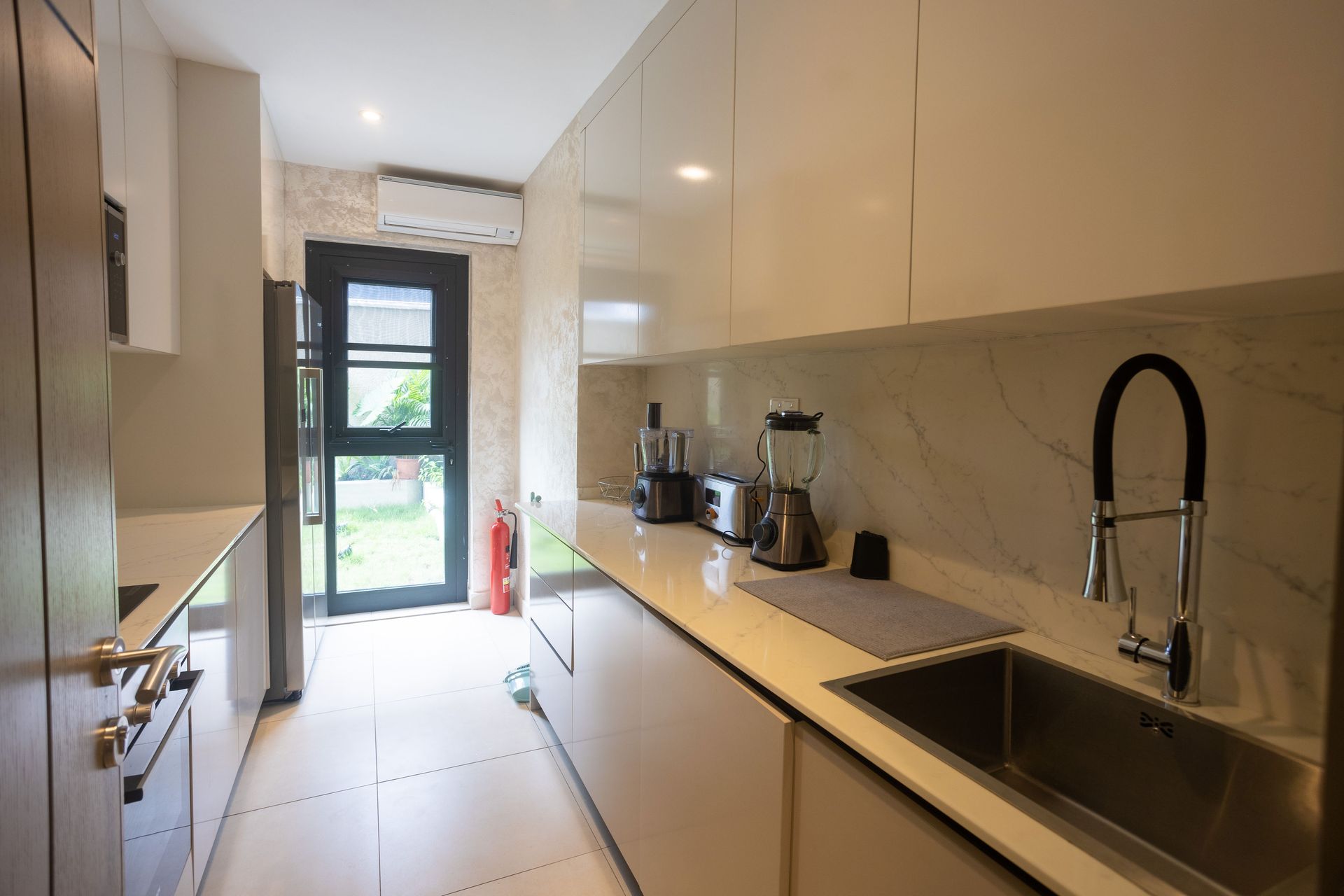 Bright modern galley kitchen with white cabinets, black sink faucet, and a door at the end.